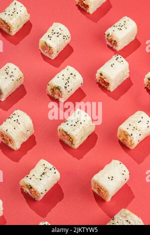 Uno scatto verticale di un sushi del rullo della mano su uno sfondo rosso Foto Stock