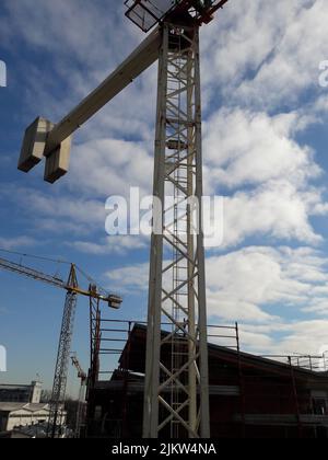 Un colpo verticale di gru a torre sul cantiere su un cielo nuvoloso blu sullo sfondo Foto Stock