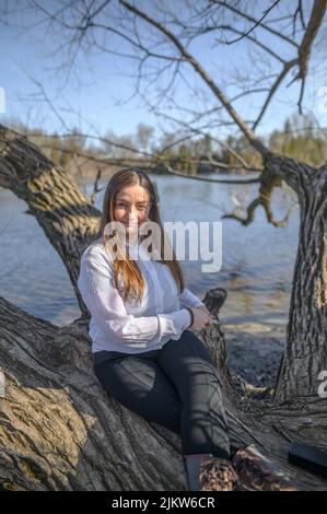 Una donna sicura all'aperto di fronte ad un fiume si siede su un ramo di albero Foto Stock