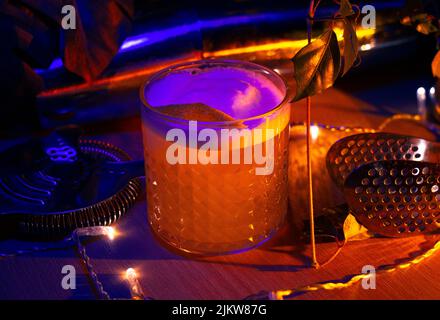 Un primo piano di un cocktail di gin fizz, una decorazione con un tocco di limone e un'attrezzatura da bar sotto la luce al neon Foto Stock