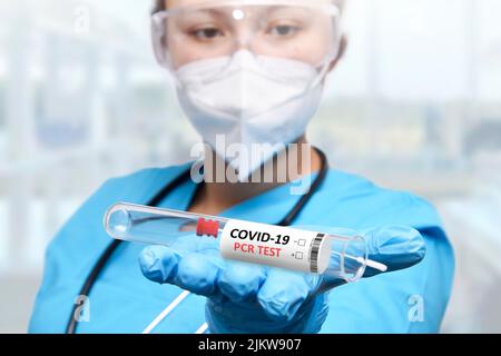 Un tecnico NHS che tiene in mano il kit di raccolta del tampone COVID-19 indossando la tuta protettiva e la maschera DPI bianche Foto Stock