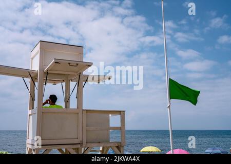 Guardia costiera di sicurezza presso la torre costiera di sicurezza, bandiera verde che indica le condizioni di sicurezza per i visitatori della spiaggia Foto Stock