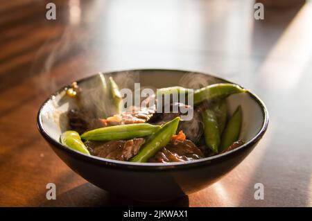 Un piatto caldo del manzo saltato con piselli in una ciotola sul tavolo di legno Foto Stock