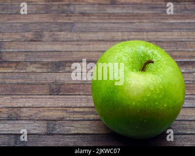 mela verde con gocce d'acqua di lille su di essa, su un angolo in basso a destra di un tavolo di legno Foto Stock