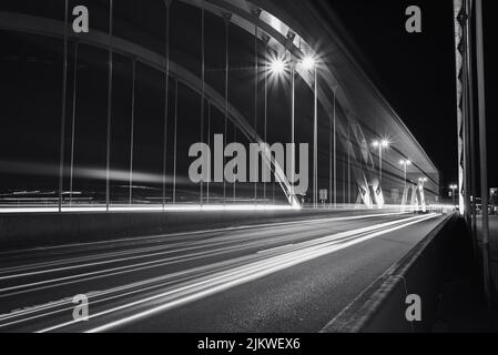 Un'immagine in scala di grigi di un ponte con un effetto di esposizione prolungato sulle luci dell'auto durante la notte Foto Stock