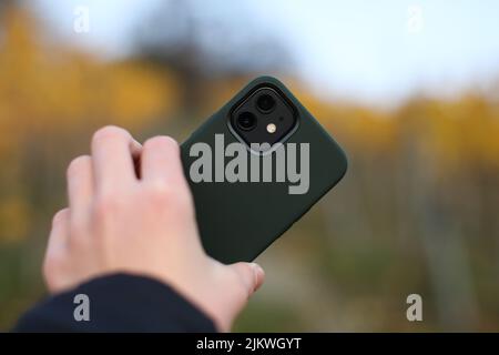 Una mano maschile che tiene uno smartphone in una custodia verde scuro su sfondo sfocato Foto Stock