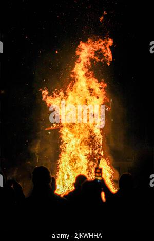 Un colpo verticale di un enorme fuoco con persone che lo circondano Foto Stock