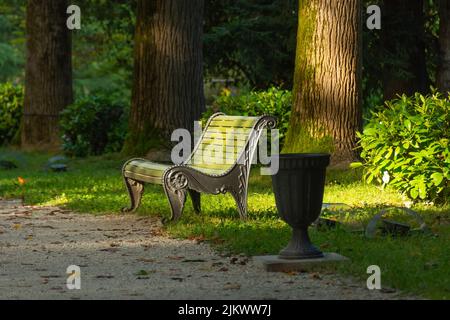 Panca verde in legno con base in metallo con un'urna vicina in un parco ombreggiato Foto Stock