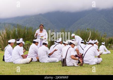 Uomini in preghiera vestiti di bianco con il tempio di pura Bratan sul lago di Bali, Indonesia Foto Stock