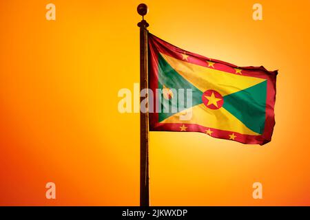 La bandiera nazionale di Grenada su un flagpole isolato su uno sfondo arancione Foto Stock