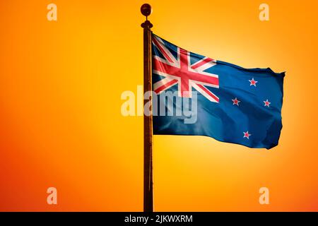 La bandiera nazionale della Nuova Zelanda su un flagpole isolato su uno sfondo arancione Foto Stock