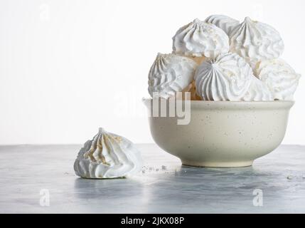 primo piano di meringa cosparsa di briciole in un piatto bianco su sfondo grigio con spazio copia, fuoco selettivo. cottura in casa. Cartolina per conf Foto Stock