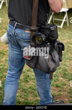 Un fotografo di giornale con fotocamere Canon e una borsa per fotocamera Domke scatta fotografie in un festival all'aperto a Santa Fe, New Mexico. Foto Stock