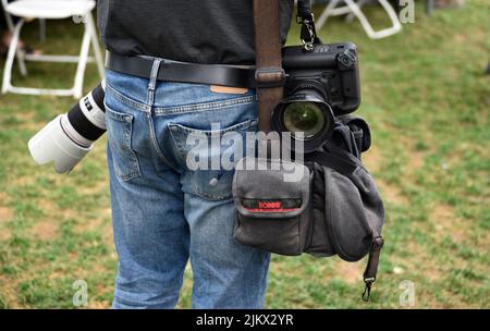 Un fotografo di giornale con fotocamere Canon e una borsa per fotocamera Domke scatta fotografie in un festival all'aperto a Santa Fe, New Mexico. Foto Stock