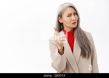 Ritratto di donna asiatica seria di mezza età che guarda severo, tremando il dito e scolding qualcuno, guardando deluso, disapprova smth, in piedi sopra Foto Stock