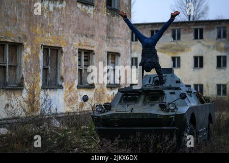 Uomo che fa una mano su un carro armato BTR nel cortile di una baracca sovietica abbandonata Foto Stock