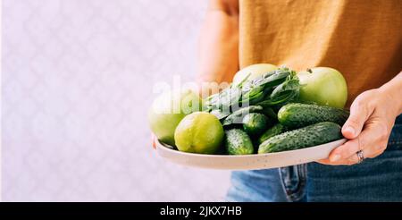 Una donna tiene nelle sue mani frutta fresca di verdure verdi in grande piatto, spazio di copia di sfondo chiaro Foto Stock