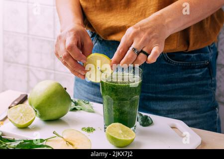 Una donna prepara una bevanda frullato verde da frutta e verdura fresca, il processo di cottura Foto Stock