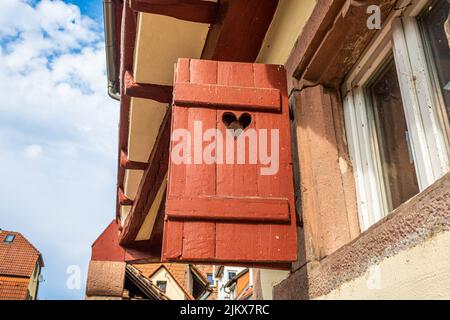 vecchia tapparella in legno rosso con buco a forma di cuore su casa a graticcio in piccola città nella germania meridionale Foto Stock