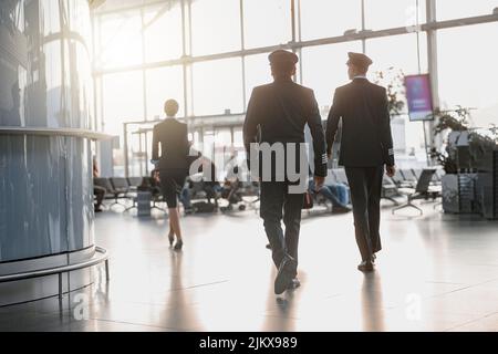 Due piloti camminano lungo il terminal dell'aeroporto seguendo la stewardess Foto Stock