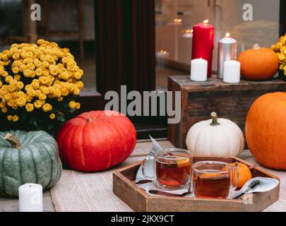 Vassoio di legno con tè speziato sul portico della casa decorato con zucche, fiori e candele. Accogliente ingresso casa decorata per vacanze autunnali. Foto Stock