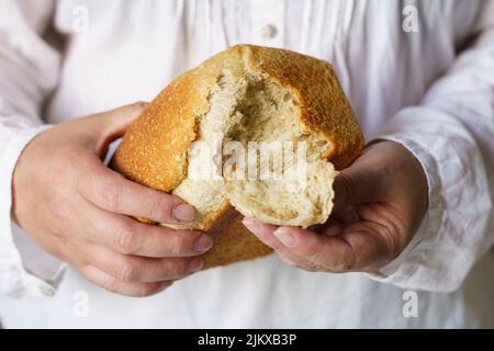 Un uomo tiene il pane cotto nelle sue mani, strappa un pezzo da esso. Cibo Foto Stock