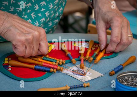 Mani di donna che fanno merletto di bobina. Fili colorati di pizzo. Abilità e creatività. Foto Stock