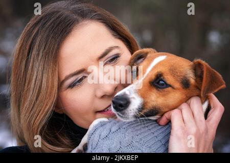 Giovane donna che tiene il suo cane terrier Jack Russell indossare abiti invernali caldi sulle mani, primo piano dettaglio Foto Stock