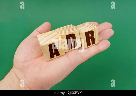 Concetto aziendale. Su sfondo verde, nelle mani di una persona, cubetti con l'iscrizione - ADR Foto Stock