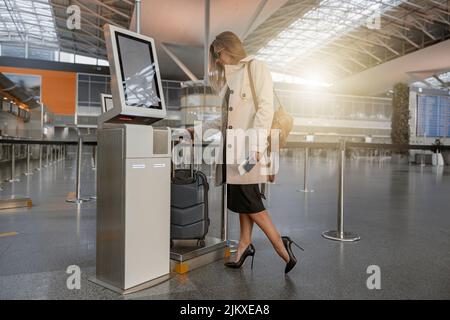 Famale turistico in piedi vicino al chiosco self check-in automatico in aeroporto Foto Stock