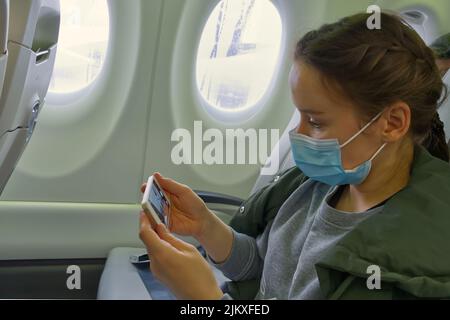 donna viaggiatore che indossa maschera per prevenire l'infezione covid-19 durante il viaggio in aereo utilizzando il telefono cellulare mentre si siede sull'aeroplano. Foto Stock