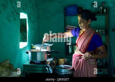 Un fuoco selettivo di una donna indiana che cucina in una cucina. Foto Stock