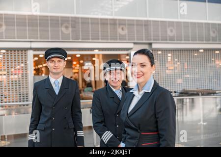 Felice due piloti e stewardess in piedi nel terminal dell'aeroporto Foto Stock
