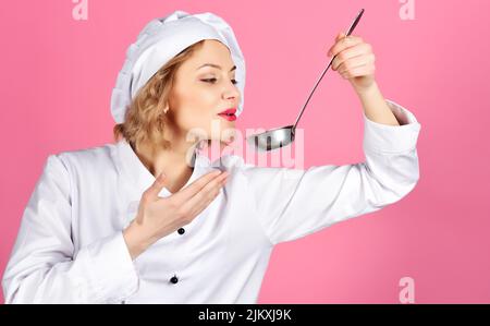 Cuoco femminile in bianco uniforme gustando cibo con cucchiaio per mestolo. Cucina e cucina professionale. Foto Stock