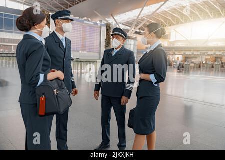 Team di aerei in maschere che parlano al terminal dell'aeroporto Foto Stock