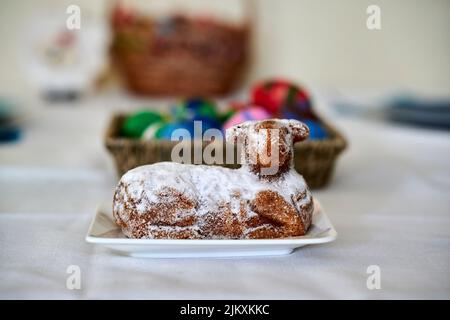 Un dessert a forma di pecora al forno su un piatto e un cesto di paglia con uova dipinte sullo sfondo Foto Stock