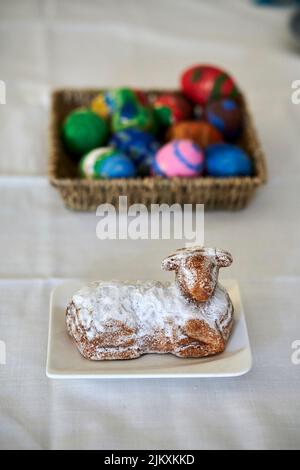 Un dessert a forma di pecora al forno su un piatto e un cesto di paglia con uova dipinte sullo sfondo Foto Stock