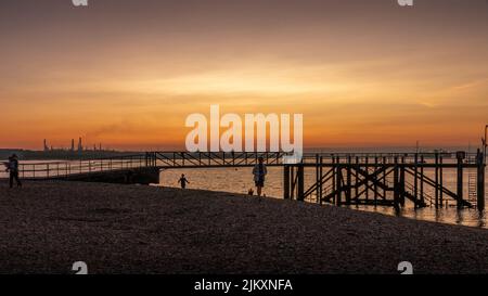 Una splendida vista del tramonto sul molo con persone che camminano sulla spiaggia Foto Stock
