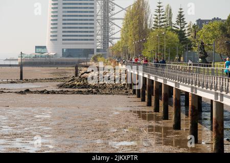 Un gruppo di persone che cammina su un ponte sul fiume Tago con la bassa marea nel Parque das Naces, Lisbona Foto Stock