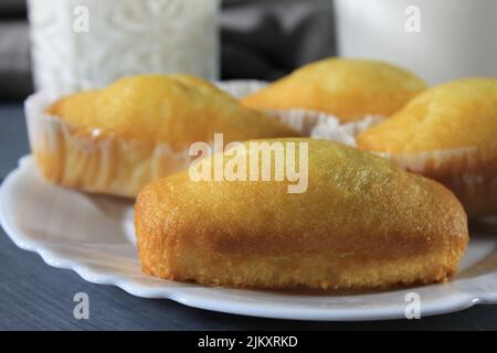 primo piano di diversi plumcake su un piatto bianco con un bicchiere di latte accanto, su un tavolo di legno grigio Foto Stock