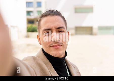 Ritratto di un giovane uomo misto che prende un selfie con uno smartphone in città Foto Stock