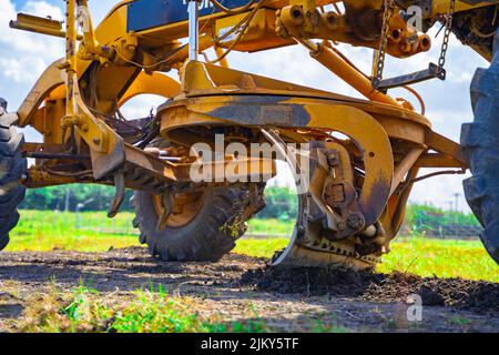 La livellatrice a terra regola la superficie stradale in modo uniforme al livello calcolato dagli ingegneri, per la costruzione di strade industriali, utilizzando lo stato dell'a Foto Stock