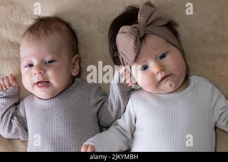 Un primo piano di due graziosi neonati sdraiati su una coperta beige Foto Stock