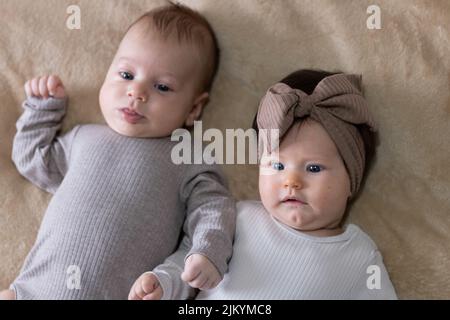 Un primo piano di due graziosi neonati sdraiati su una coperta beige Foto Stock