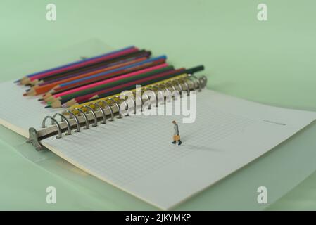 Un primo piano di un notebook con matite colorate e una statuetta di un uomo sul concetto IT di conoscenza Foto Stock