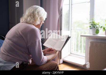 Donna anziana che riposa sul divano e legge un libro Foto Stock