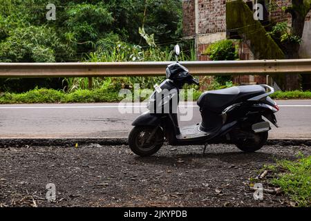 Kolhapur, India- Settembre 13th 2019; foto d'archivio scooty colore nero o scooter parcheggiato sul lato della strada. Asfalto vuoto e alberi verdi sul dorso Foto Stock