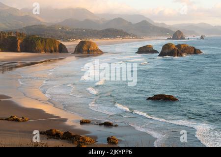 La luce del sole in tarda serata cade attraverso Cannon Beach e il mare si impila sull'Oregon Cost lungo l'Oceano Pacifico Foto Stock