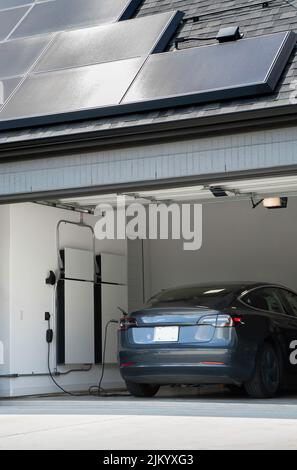 Veicolo elettrico Charing in un garage con generatori di batteria di riserva alimentati da pannelli solari su un tetto Foto Stock
