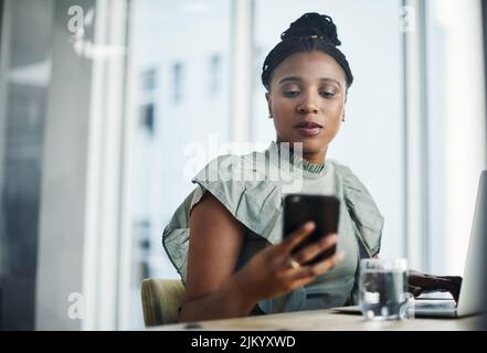 Piuttosto sono occupato che annoiato. Una giovane donna d'affari attraente seduta in ufficio e usando il suo cellulare e il suo portatile. Foto Stock